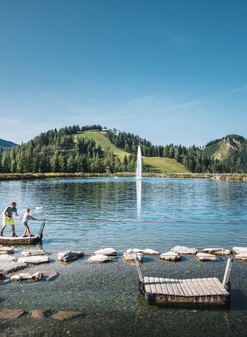 Ein Mann fährt mit seinem Sohn während ihres Wanderurlaubs in Österreich mit einem Floß über einen See.
